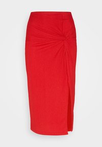 Jupe midi rouge ajustée en tissu côtelé, dotée d'un détail en nœud torsadé à la taille et d'une fente sur le côté pour plus de liberté de mouvement.