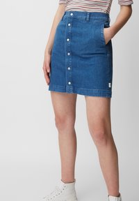 Jupe en denim bleu moyen, présentant une coupe ajustée, une fermeture à boutons à l'avant, deux poches latérales et un ourlet qui tombe au-dessus du genou.