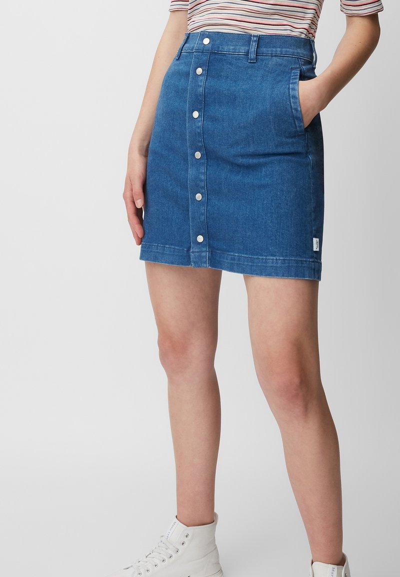 Jupe en denim bleu moyen, présentant une coupe ajustée, une fermeture à boutons à l'avant, deux poches latérales et un ourlet qui tombe au-dessus du genou.