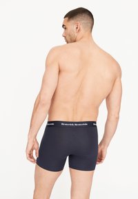 Boxers de color azul marino hechos de tela suave con una cinturilla texturada que presenta una marca blanca. Tienen un diseño ajustado y una longitud hasta mitad del muslo.