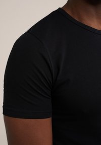 Camiseta corta negra de manga corta fabricada con un tejido liso y elástico. Presenta un escote redondo y un diseño ajustado, con costuras y puntadas visibles.