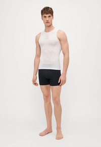 Débardeur en compression blanc sans manches avec des panneaux en maille et un col arrondi, associé à un short noir ajusté. Texture lisse, design minimaliste.