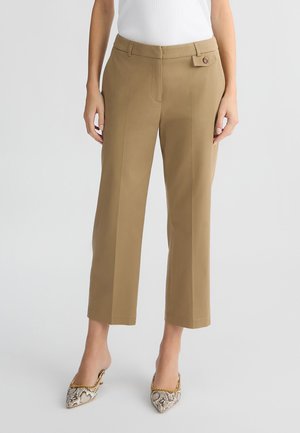 Pantaloni cropped color khaki con vestibilità sartoriale, chiusura a singolo bottone, tasche laterali e texture liscia. Abbinati a décolleté a pianta con motivo.