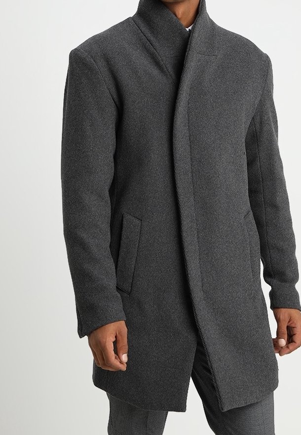 Homme portant un manteau en laine gris foncé avec un col montant et une fermeture avant dissimulée, debout devant un fond clair uni.