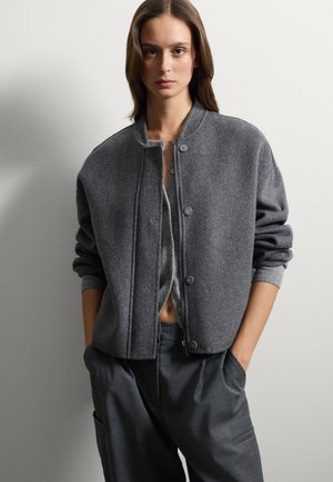 Veste bomber en laine grise avec un col rond, une fermeture à boutons et des poignets côtelés. Assortie à un pantalon gris à coupe ample.