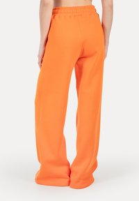 Pantaloni della tuta arancioni con vestibilità ampia ed elastico in vita. Tessuto morbido, gambe larghe che si stringono alla caviglia.