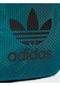 Torba w kolorze morskim z wzorem heksagonalnym, z czarnym logo Adidas i trzema czarnymi paskami. Wykonana z teksturowanego materiału o gładkim wykończeniu.