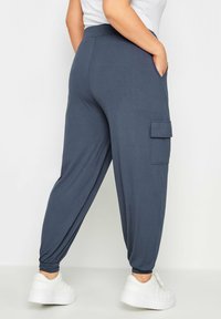 Person som bär mörkblå joggingbyxor med ankelslitsar och sidofickor, tillsammans med vita plattformsskor och en vit topp.