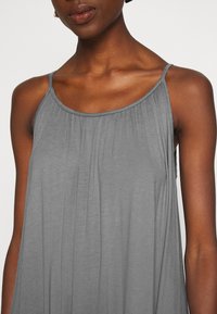 Grå ärmlös klänning med plisserad tyg, mjuk textur och tunna axelband, med en avslappnad passform som faller över axlarna.