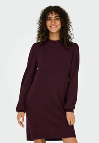 Vestito a maglia bordeaux con maniche lunghe a palloncino e collo alto. Texture liscia, corpetto aderente e silhouette ampia all'orlo.