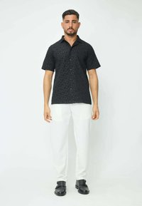 Chemise noire à manches courtes avec un motif géométrique texturé, accompagnée d'un pantalon blanc à jambe droite et de chaussures noires à enfiler.