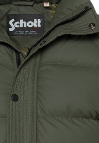 Giacca a vento verde con design trapuntato, dotata di chiusura a zip, bottoni a scatto e etichetta interna nera con informazioni sul marchio.