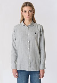 Camicia a righe con bottoni nera e bianca, con maniche lunghe, colletto e un piccolo logo ricamato sul petto. Materiale in cotone.