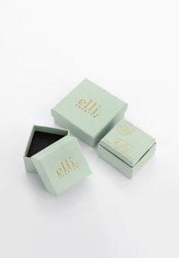 Lysegrønne kasser med guldtekst; én åben, som viser en sort inderside. Den mindre kasse passer ind i den større, begge lavet af papir.