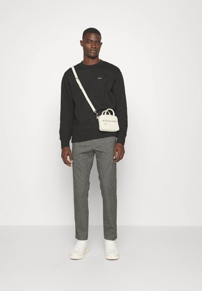 Schwarzes Sweatshirt, graue maßgeschneiderte Hose, weiße Sneakers und eine kleine weiße Umhängetasche. Einfaches Design mit minimalen Details und kontrastierenden Farben.