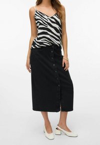 Falda de mezclilla negra con botones en la parte frontal, con un corte recto y una abertura. Combinada con una camiseta de tirantes con estampado de cebra en blanco y negro y zapatos blancos.