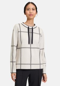 Beige pullover sweater with black grid pattern, featuring a rounded neckline and black drawstrings, made of a textured knit fabric.