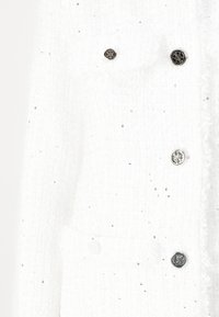 Chaqueta de tweed blanca con botones plateados y sutiles decoraciones. Presenta una tela texturizada y un diseño estructurado.