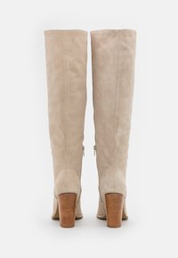 Beige suède laarzen tot de knie met een recht ontwerp, zijritsen en houten blokhakken. Soepele textuur met nette stikdetails.