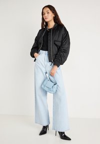 Μαύρο σατέν bomber μπουφάν, μαύρο τοπ, ανοιχτό μπλε ψηλόμεσο τζιν παντελόνι με φαρδιά πόδια, μπλε τσάντα και μαύρες μυτερές γόβες.