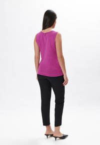 Top senza maniche fucsia con scollo rotondo e un piccolo dettaglio con bottone sul retro, abbinato a pantaloni neri a sigaretta e mule nere.