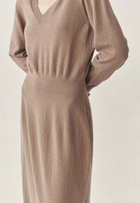 Garas brūnas krāsas kleita no mīksta adīta auduma. Tai ir V veida izgriezums, garas piedurknes un pieguļoša vidukļa daļa, kas pāriet vaļīgā svārkos.