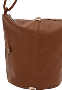 Brun læder bucket taske med sølv hardware, lynlåslukning og to udvendige lommer. Designet har synlige syninger og en afrundet form.
