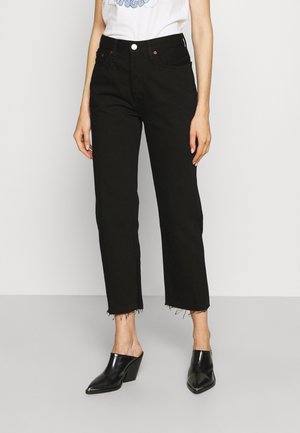 Kvinde iført sorte højtaljede straight-leg cropped jeans med rå kanter, hvid grafisk t-shirt og sorte spidse hælede mules.
