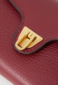 Borsa a mano in pelle rossa con superficie testurizzata, chiusura in metallo dorato e design a patta curva. Presenta un dettaglio di marchio in rilievo.