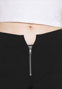 Calções pretos de cintura alta com fecho e um recorte na frente. Tecido suave com uma textura lisa e um design minimalista.