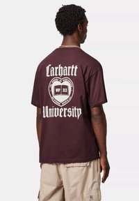 Camiseta de algodón color burdeos con un gran gráfico blanco en la parte posterior que muestra el texto "Carhartt University" y un emblema con un libro abierto.