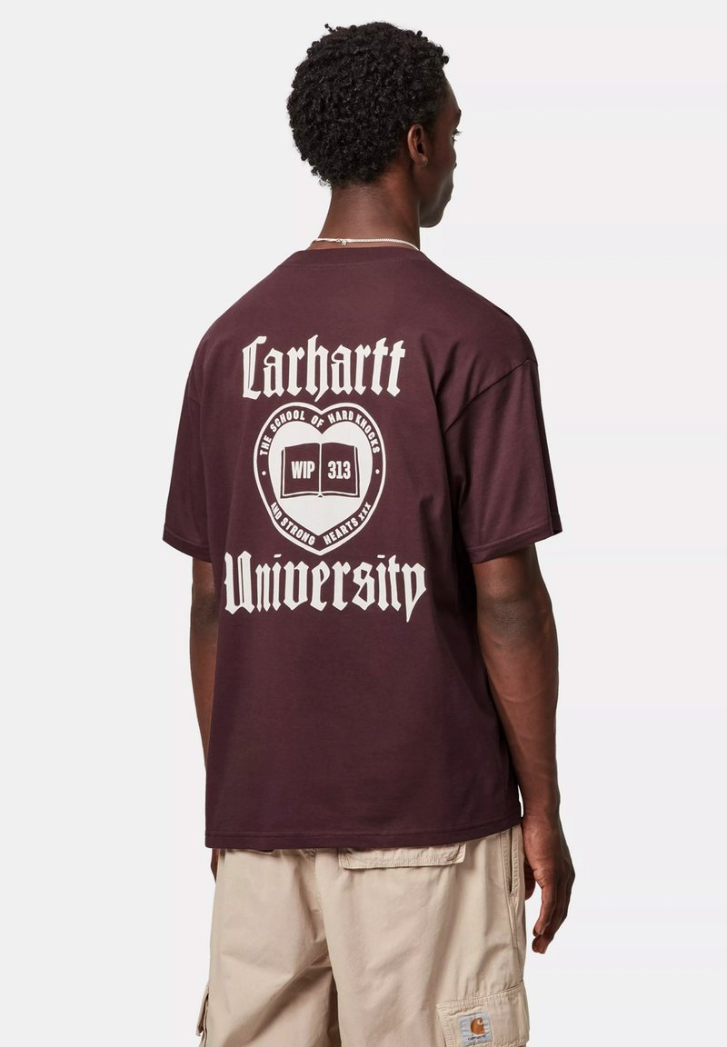 T-shirt in cotone marrone scuro con una grande grafica bianca sulla schiena, recante il testo "Carhartt University" e un emblema con un libro aperto.