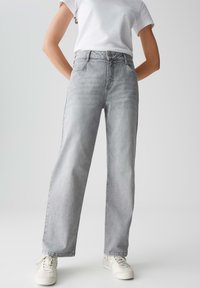 Jeans in denim grigio con vita alta, taglio dritto, sbiadimenti leggeri e cinque tasche. Abbinati a sneakers bianche e una t-shirt bianca semplice.