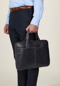 Sort læder laptop arbejdstaske med to top-h�åndtag, lynlås lukning og en glat overflade. Pænt struktureret med subtile stikningsdetaljer.