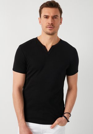 Schwarzes Kurzarm-T-Shirt mit V-Ausschnitt und drei braunen Knöpfen am Hals. Glatter Stoff und figurbetonter Schnitt.