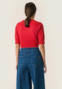 Rød ribbet t-shirt med korte ærmer parret med blå brede jeans med høj talje og to baglommer. Glat tekstur og levende farver.