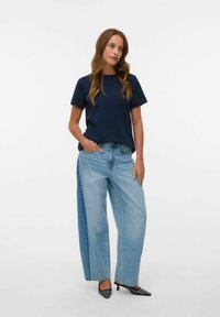 Marineblå kortærmet t-shirt sat sammen med brede lyseblå jeans med rå kant. Accentueret med sorte højhælede sko med hvide mønsterdetaljer.