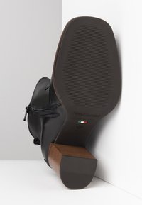 Stivale alla caviglia in pelle nera con chiusura a zip, dotato di suola in gomma testurizzata e tacco in legno a contrasto. Presenta dettagli del marchio.