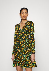 Vestido preto envolvente com mangas longas, apresentando um padrão vibrante de cerejas amarelas e verdes e uma saia rodada com uma bainha ondulada.