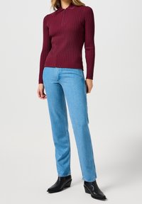 Bordowa, prążkowana bluzka z długim rękawem i zamkiem przy szyi, w zestawie z jasnoniebieskimi, prostymi jeansami oraz czarnymi botkami na koturnie.