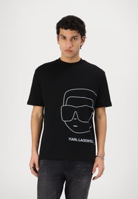 Black cotton t-shirt featuring a white outline graphic of sunglasses and a face, with "KARL LAGERFELD" printed beneath. Standard fit.
