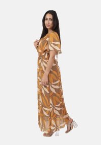Vestido maxi en una tela ligera y transparente con un estampado abstracto de hojas en tonos marrón, naranja y crema; cintura ceñida, mangas cortas y diseño fluido.