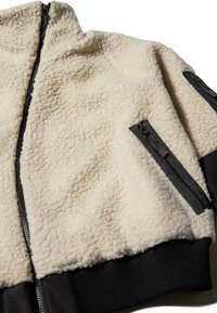 Giacca in pile con parte superiore color crema dal tocco morbido, sezione inferiore nera, tasche laterali con zip e design collo stand.