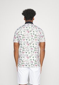 Polo à manches courtes blanc avec un motif floral et de flamants roses éclatant ; doté d'un col noir ; fabriqué en tissu lisse.