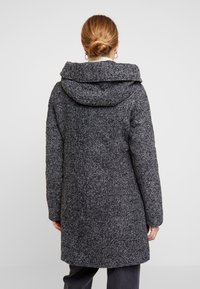 Cappotto grigio texturizzato con un ampio cappuccio, maniche lunghe e un design di lunghezza intermedia. Presenta un motivo screziato per un tocco di dettaglio aggiuntivo.