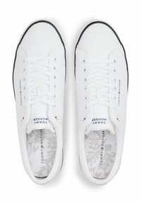 White canvas sneakers with a textured upper, round toe, black sole, and laces; featuring "Tommy Hilfiger" logo and a patterned insole.