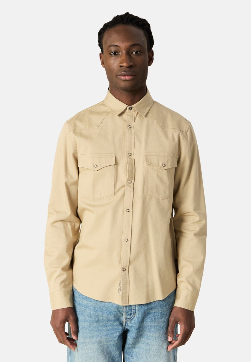 Camicia beige a maniche lunghe con colletto button-down, due tasche sul petto e bottoni in metallo. Tessuto morbido con una texture liscia.