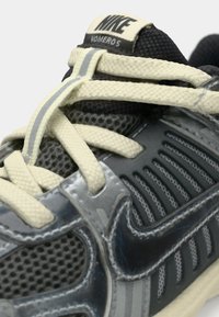 La sneaker Nike Vomero presenta una tomaia in mesh in tonalità di grigio con accenti riflettenti, lacci crema e un colletto imbottito per il comfort.