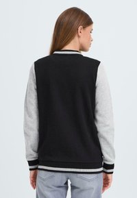 Sort og grå varsityjakke med lange ærmer, ribbet manchetter og kant. Funktioner et minimalistisk design med kontrasterende farver.