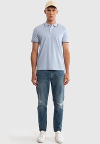 Polo de color azul claro con corte ajustado, con un contraste en el cuello, combinado con jeans destrozados de color azul claro y zapatillas blancas.